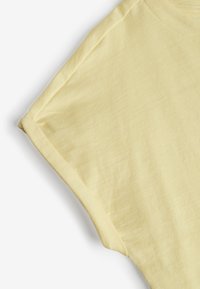 Camiseta de color amarillo claro con escote redondo, mangas cortas dobladas y textura suave. La tela parece ligera y casual.