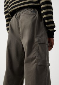 Cargo bukser i lysegråt stoff har en avslappet passform, elastisk midjebånd og sidelommer. Designet inkluderer subtile sømdetaljer.