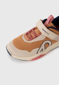 Baskets brunes avec des accents beige, lacets élastiques roses et une sangle réglable beige étiquetée "reima TEC" sur un fond blanc.