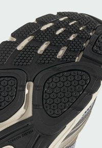 Shoe outsole featuring a black rubber design with circular tread patterns, textured sections, and a visible "TORSION SYSTEM" label.