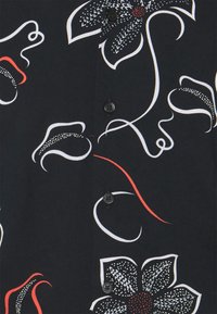 Short-sleeve shirt in black fabric featuring white, red, and green floral patterns with intricate details and black buttons down the front.