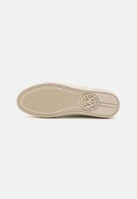 Suola di scarpa in gomma beige con superficie testurizzata e logo circolare. Presenta linee orizzontali e una leggera curvatura lungo i bordi.