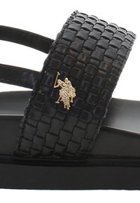 Černé tkané kožené sandály se dvěma řemínky, s hladkou černou podrážkou a metalickým zlatým logem na horním řemínku.