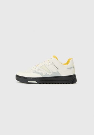 White and grey athletic shoe with a textured upper, yellow accents on the tongue, and a thick black sole. Features perforations for breathability.