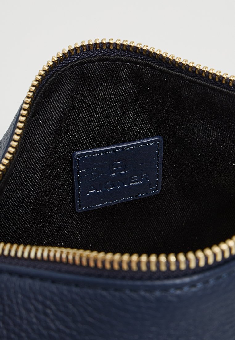 Navy Leder Tasche Innenraum mit einem goldenen Reißverschluss, ausgestattet mit einem strukturierten schwarzen Futter und einem blauen Leder-Logo.