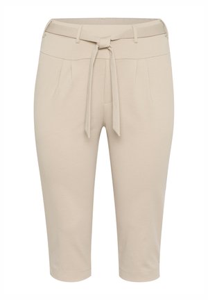 Pantalons croisés beiges ajustés, avec une taille ceinturée, des plis latéraux et un tissu lisse. Ils se terminent au-dessus de la cheville avec une coupe droite.