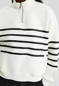 Pullover in felpa bianca con colletto a mezza zip, caratterizzato da audaci strisce orizzontali nere sul petto e sulle maniche. Texture morbida.