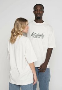 Přiléhavé bílé trička ve velkém provedení vyrobená z měkké látky s kulatým výstřihem. Na přední straně je grafika "Multiply Apparel" v tmavě zelené barvě. Volný střih, krátké rukávy.