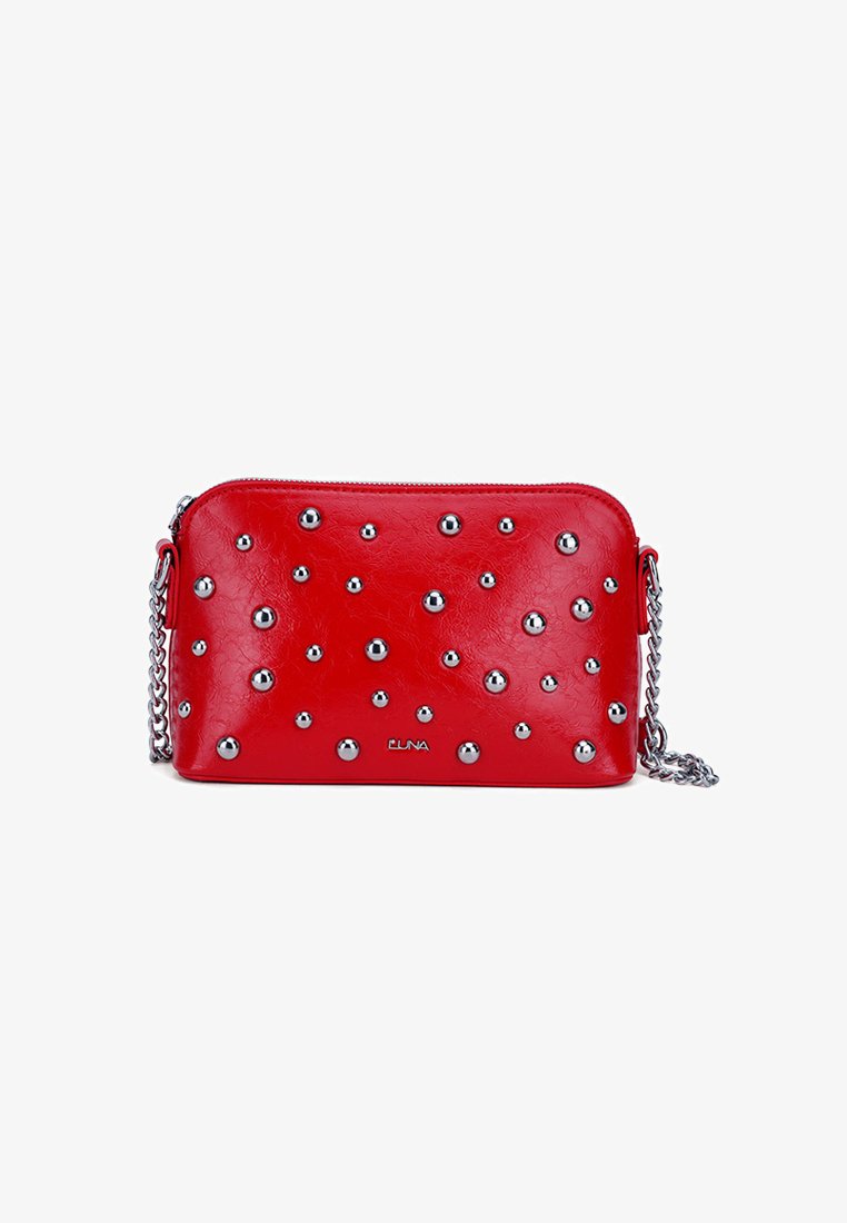 Bolso cruzado de imitación piel roja con tachuelas plateadas, cierre de cremallera y correa de cadena. Textura suave, forma rectangular, con marca notable en la parte frontal.
