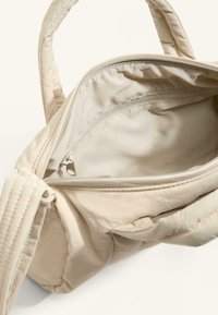 Jasnobeżowa torebka o pikowanej fakturze, z kieszenią wewnętrzną na zamek i materiałową podszewką. Krótkie uchwyty i miękki materiał.