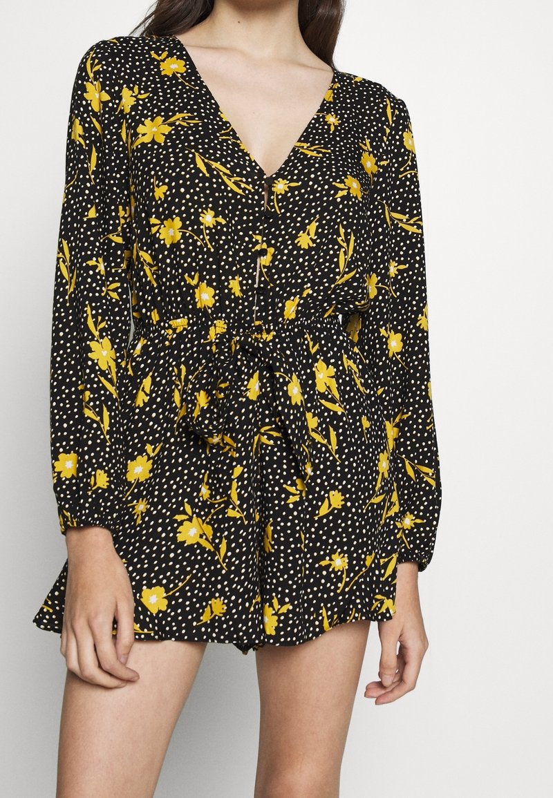 Vestido negro con estampado floral que presenta flores amarillas y lunares blancos, de mangas largas, escote en V profundo, y cintura elástica con detalle de lazo.