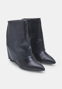 Stivali alla caviglia con zeppa in pelle nera, punta affusolata, texture liscia e design a risvolto. Suole robuste e dettagli cuciti sulle cuciture.