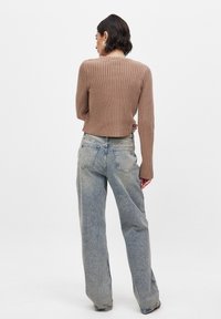 Brun ribbad stickad tröja med långa ärmar, kombinerad med ljustvättade, löst sittande jeans, sedd bakifrån mot en enfärgad bakgrund.