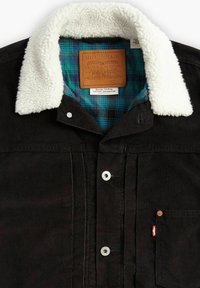 Black corduroy jacket with a white fleece collar, green and blue plaid lining, silver hardware, and a leather label. Front chest pocket included.