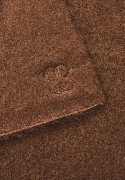 Brun filtstof med en blød tekstur, der har et prægning af et blomsterlogo i hjørnet. Kanterne har en ren finish.