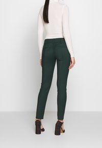 Skräddarsydda gröna byxor med smal passform, slät front och två bakfickor, tillsammans med en kroppsformad långärmad topp och klackar med rutmönster.