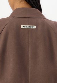 Ruskea takki, jossa on teksturoitu kangas. Varustettu viilto-kauluksella ja takana on "PATRIZIA PEPE" -tunnus.
