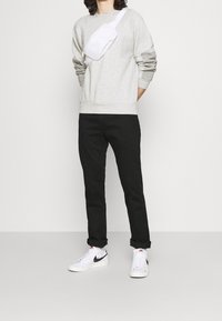 Grå sweatshirt, svarta byxor och vita sneakers. Modellen bär en vit axelremsväska. Avslappnad, ledig passform med ribbade muddar vid ärmarna.