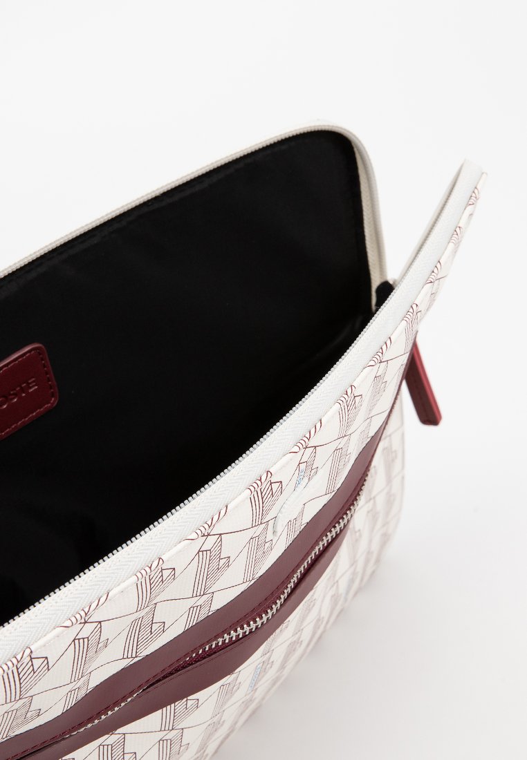 Pochette en toile avec une surface blanche ornée d'un motif géométrique rouge et bleu. Fermeture zippée avec une finition en cuir bordeaux. Doublure intérieure noire.