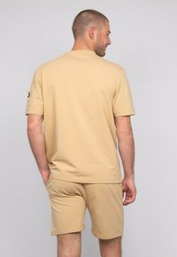 T-shirt en coton beige à manches courtes, col rond ; associé à un short beige assorti, les deux présentant une texture lisse.