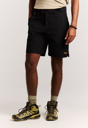 Zwarte shorts gemaakt van duurzaam materiaal, met een losse pasvorm, zijzakken en een klein logodetail aan de linkeronderkant. Gecombineerd met wandelschoenen.