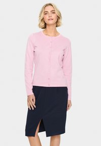 Svetlo roza pleteni kardigan z dolgimi rokavi in sprednjimi gumbi, v kombinaciji z mornarsko krilom, ki ima stranski razporek in žepe.