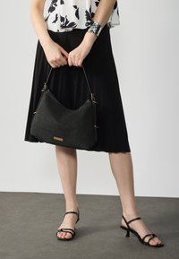 Geantă hobo împletită neagră cu accesorii aurii; suprafață texturată; completată cu o fustă plisată neagră și sandale negre cu bretele.