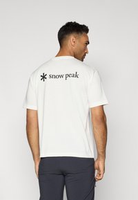 White cotton t-shirt featuring a black logo on the back, short sleeves, a round neck, and a relaxed fit.