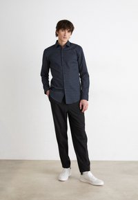 Marineblå skjorte med hvitt geometrisk mønster, lange ermer, enkelt brystlomme, parret med svarte bukser og hvite sneakers.