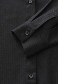 Camicia scura a righe con maniche a polsino abbottonato e bottoni visibili lungo la parte anteriore.