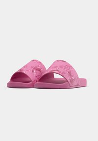 Pink slide sandals with a smooth texture, wide straps featuring a swirl pattern, and sturdy flat soles designed for comfort.