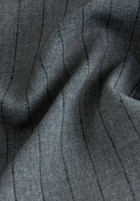 Gros plan d'un tissu gris foncé avec de subtiles rayures verticales et des plis doux créant des motifs d'ombre texturés.