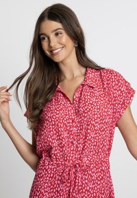 Kurzes, knopfbares Kleid mit kurzen Ärmeln in leuchtendem Rot mit einem rosa gepunkteten Muster. Verfügt über eine gebundene Taille und ein Kragen-Design für einen lässigen Sitz.