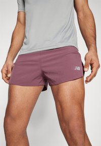 Shorts de sport courts dans une couleur prune profonde, fabriqués en un matériau léger et texturé, dotés d'un petit logo blanc de la marque sur le côté.