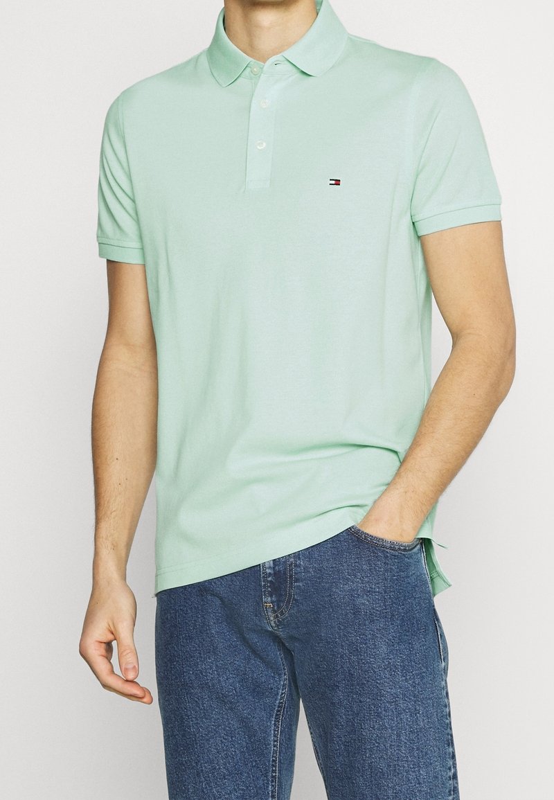 Polo shirt vert menthe en tissu mélangé coton, avec un col classique, une patte de boutonnage à trois boutons et un petit logo sur la poitrine. Associé à un jean bleu.