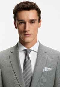 Jasnoszara marynarka z teksturą, na białej koszuli, zestawiona z szarą krawatem w paski i wzorzystą poszetką.