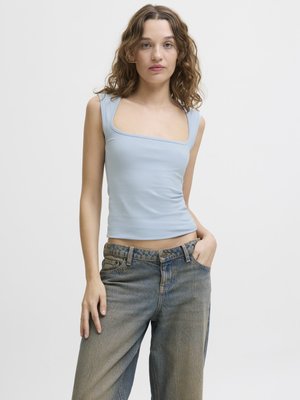 Débardeur ajusté bleu clair avec un décolleté carré, associé à un jean en denim bleu ample avec une texture délavée et un design classique à cinq poches.