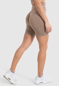 Bruine sportshorts met een hoge taille, nauwsluitend ontwerp en een gladde textuur. Gecombineerd met witte sneakers met zichtbare demping.