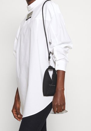 Valkoinen pitkähihainen paita, jossa on korkea kaulus ja etiketti, yhdistettynä pieneen mustaan verkkokassiin, jossa on kahva, ja säihkeä hopealukko.