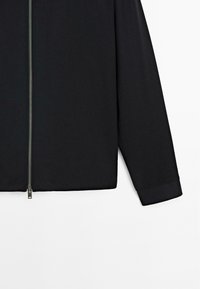 Black long-sleeve jacket with silver front zipper partially open, displayed against a plain white background.