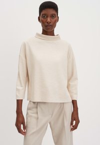 Top oversized beige chiaro con colletto alto, maniche a 3/4, texture a coste e forma quadrata, abbinato a pantaloni tailored beige chiaro.