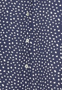 Camicia blu navy con un motivo a macchie di forme bianche irregolari, con chiusura a bottoni e una texture di tessuto liscia.