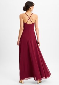 Bordeaux maxi-jurk met een aansluitend lijfje, dunne gekruiste bandjes en een vloeiende rok van lichtgewicht stof. Ritssluiting aan de achterkant.