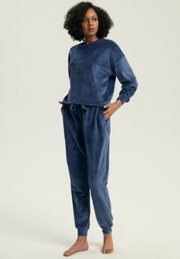 Granatowy zestaw dresowy z weluru, składający się z bluzki z długim rękawem oraz spodni z elastycznym pasem i sznurkiem. Miękka faktura, luźny krój.
