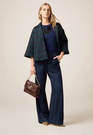 Chaqueta de mezcla de lana a cuadros en verde oscuro y negro, blusa azul marina con detalles de lentejuelas, pantalones de mezclilla de pierna ancha y bolso de cuero marrón. Accentos dorados.