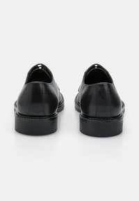 Zapatos de cuero negro con un acabado suave, punta redonda, perfil bajo y un tacón grueso. Presentan un diseño minimalista sin herrajes visibles.