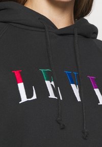Felpa nera con ricamo "LEVI" in lettere colorate: rosso, verde, bianco, blu e viola. Presenta un cordino sul cappuccio.