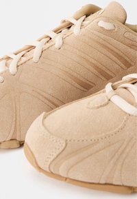 Beezsuede kingad tekstuuriga pinnaga, mis sisaldavad tonaalseid triibusid, ümmargust varvast ja kummist tallasid. Paelad on sobivas beežis.