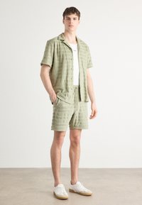 Groen gestreepte korte mouwen shirt, bijpassende shorts, van katoen, ontspannen pasvorm, met zakken aan de voorkant, gecombineerd met witte sneakers.