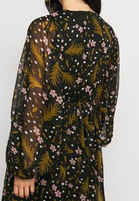Černé šaty s průhlednou látkou, zdobené květinovým vzorem v růžové a hořčicové barvě, s dlouhými nabíranými rukávy, elastickým pasem a kulatým výstřihem.